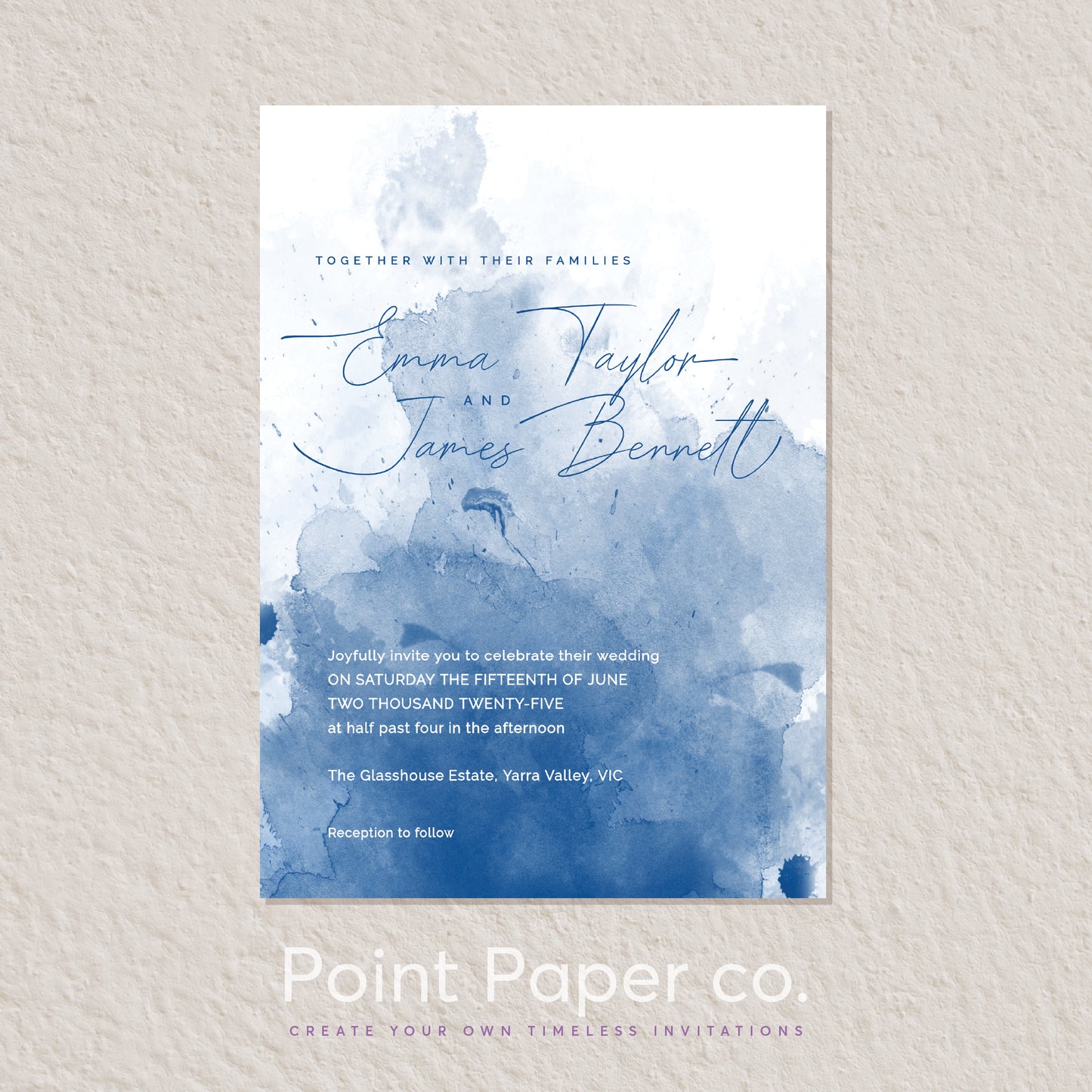 A vertical wedding invitation card with a white and blue watercolor design, displayed on a light textured wall. The card features elegant cursive names and event details, with the brand name 'Point Paper co.