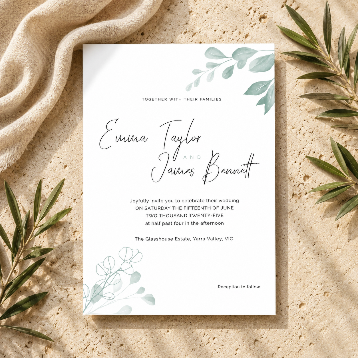 A rectangular wedding invitation card with elegant black script text and soft green botanical illustrations, styled flat on a sandy surface with draped beige fabric and olive branches around it.