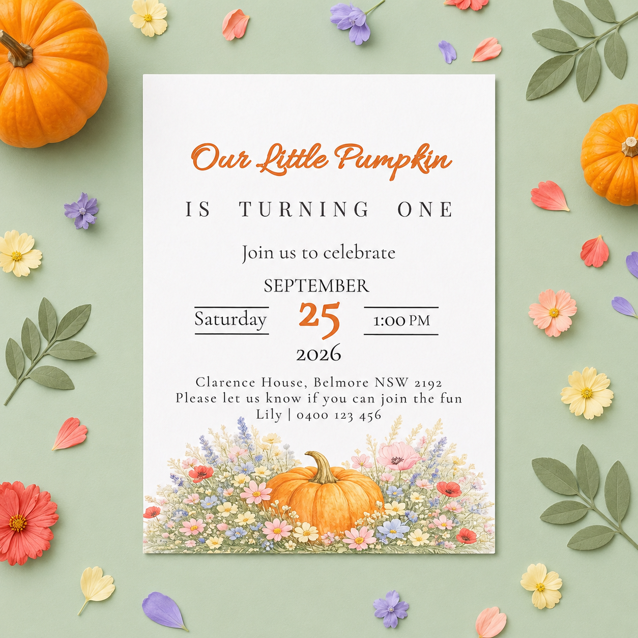 A fall-themed baby birthday invitation card styled in a flat-lay arrangement on a sage green background with scattered autumn leaves, small pumpkins, and colorful flowers. The card features orange and black text reading 'Our Little Pumpkin IS TURNING ONE' with the date 'September 25, 2026' and a watercolor illustration of a pumpkin and wildflowers at the bottom.