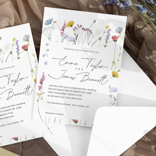 Floral wedding invitation cards with elegant script text, arranged on a rustic brown fabric surface with an open white envelope and dried flowers in the background.