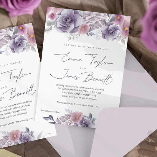 Watercolor floral wedding invitation cards with purple and lavender flowers, shown with an envelope on a soft neutral fabric background.