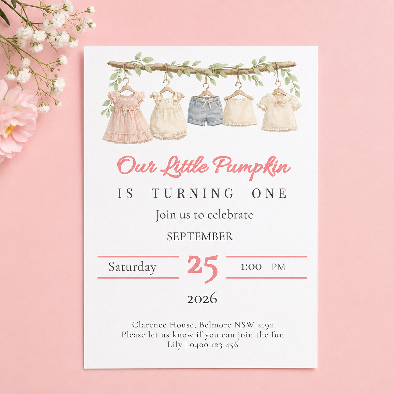 A baby first birthday invitation card styled on a pink background with white flowers. The card features watercolor illustrations of four baby dresses hanging on a clothesline, with the text 'Our Little Pumpkin IS TURNING ONE' in pink and black lettering.