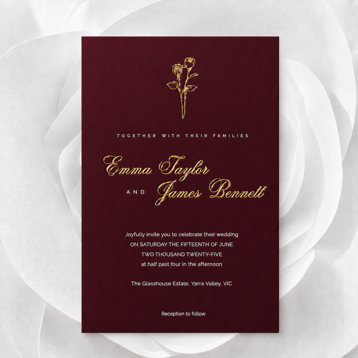 A rectangular wedding invitation card with a deep burgundy background and elegant gold typography, centered on a white floral backdrop. The card includes a small gold rose illustration at the top and names Emma Taylor and James Bennett.