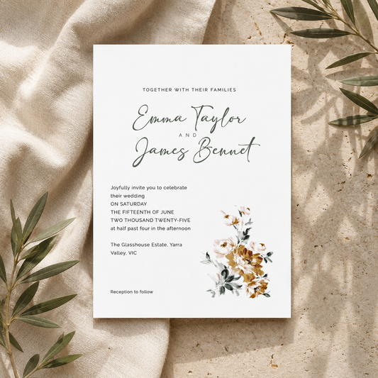 A wedding invitation card with elegant black script and floral watercolor accents, styled flat-lay on a textured beige fabric with olive leaves.