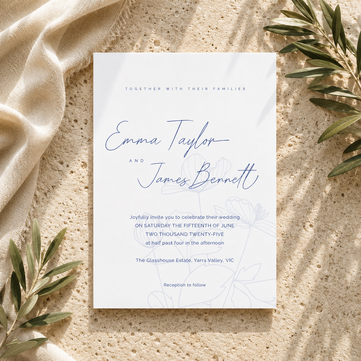 A wedding invitation card with elegant blue script and floral line art, styled flat-lay on a textured beige stone surface with draped cream fabric and olive branches.
