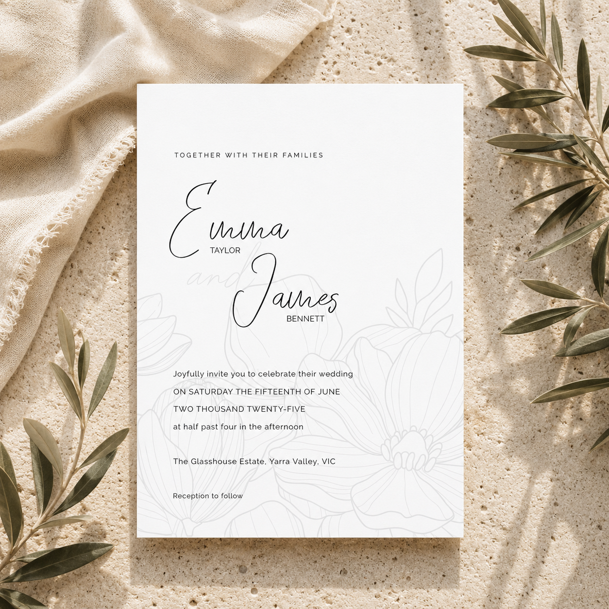 A white wedding invitation card with elegant black script and faint floral line art, styled on a textured beige surface with draped cream fabric and olive branches around it.