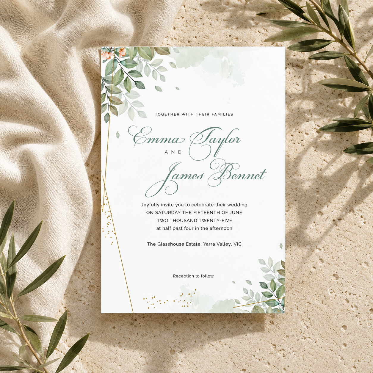 A floral wedding invitation card with elegant script text, displayed on a textured beige surface with draped cream fabric and olive leaves around it.