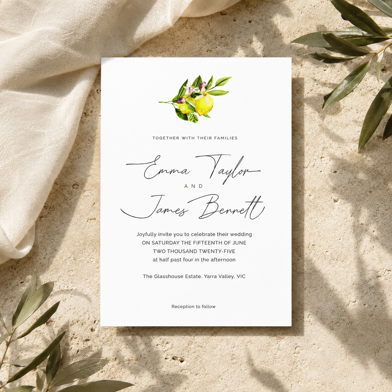 A vertical wedding invitation card with elegant black script and serif text, topped with a small watercolor lemon and olive branch illustration, styled on a textured beige surface with draped cream fabric and green leaves.