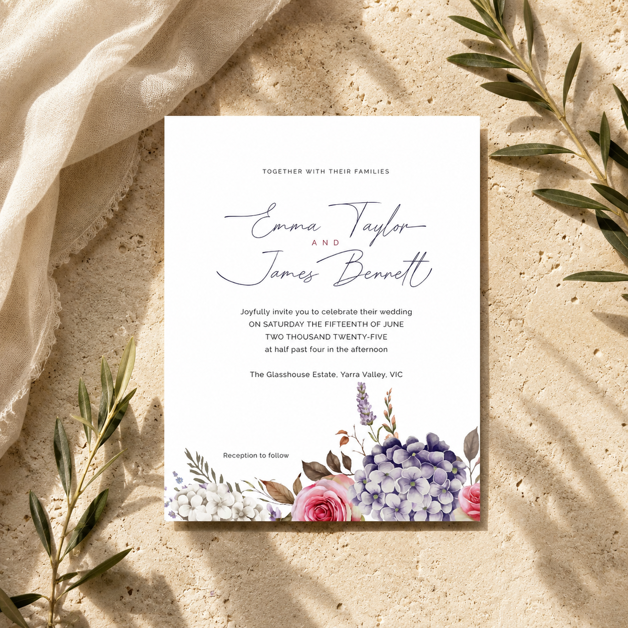 A rectangular wedding invitation card with elegant script and floral watercolor accents at the bottom, styled on a textured beige surface with draped fabric and olive branches.