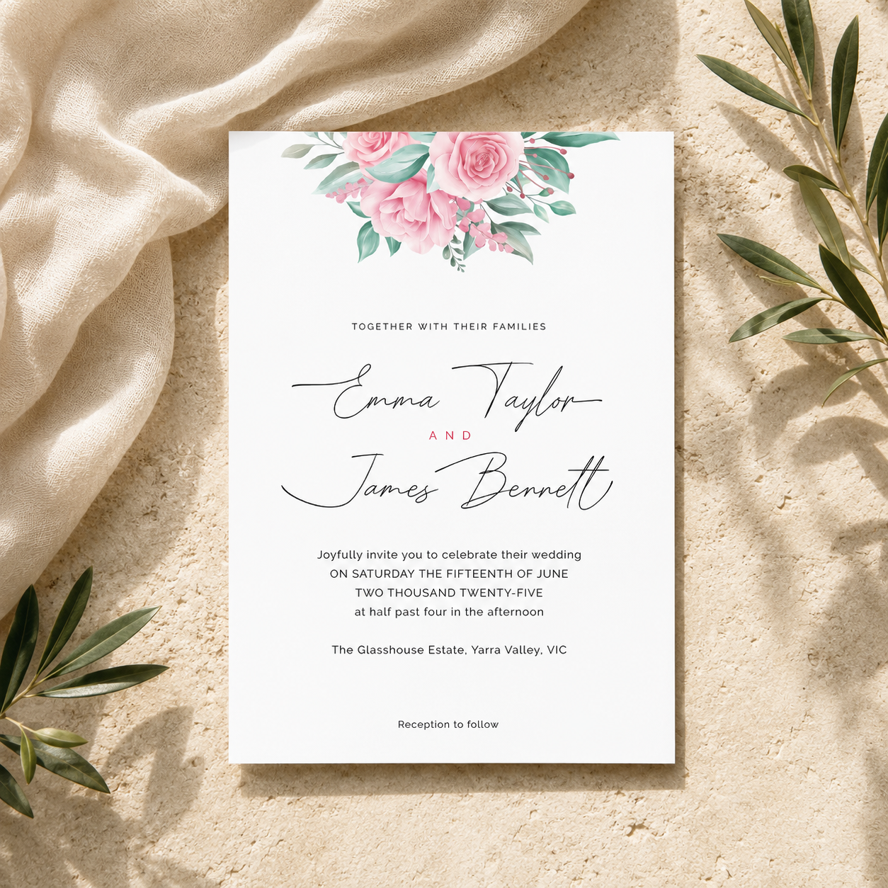 A square wedding invitation card with a watercolor floral design at the top, styled flat-lay on a textured beige surface with draped cream fabric and green leaves.
