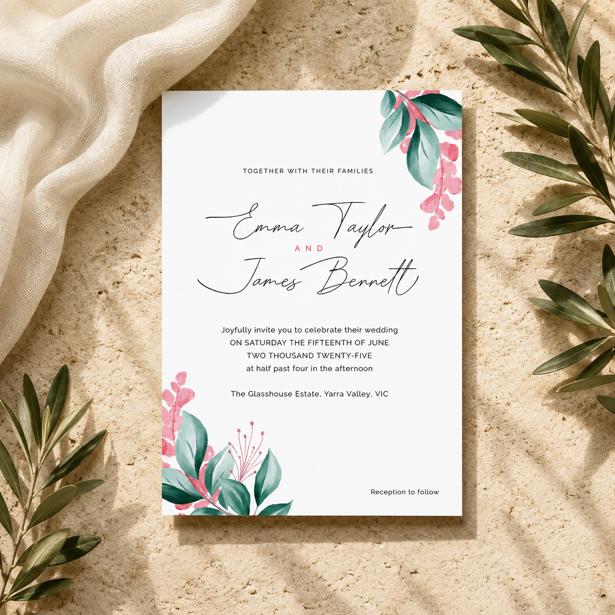 A square wedding invitation card with elegant black script and floral watercolor accents in teal and pink, styled flat-lay on a textured beige surface with draped cream fabric and green leaves around it.