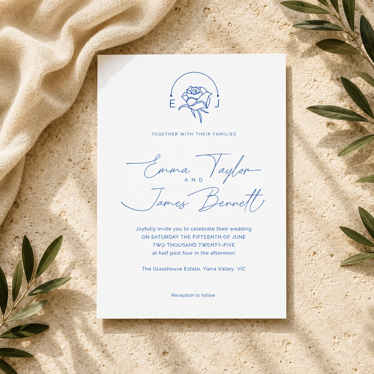 A square wedding invitation card with elegant blue typography and a rose illustration, styled flat-lay on a textured beige surface with draped cream fabric and olive leaves.