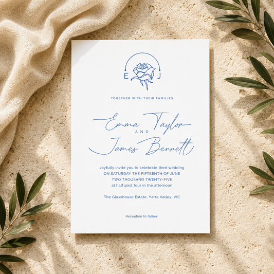 A square wedding invitation card with elegant blue typography and a rose illustration, styled flat-lay on a textured beige surface with draped cream fabric and olive leaves.