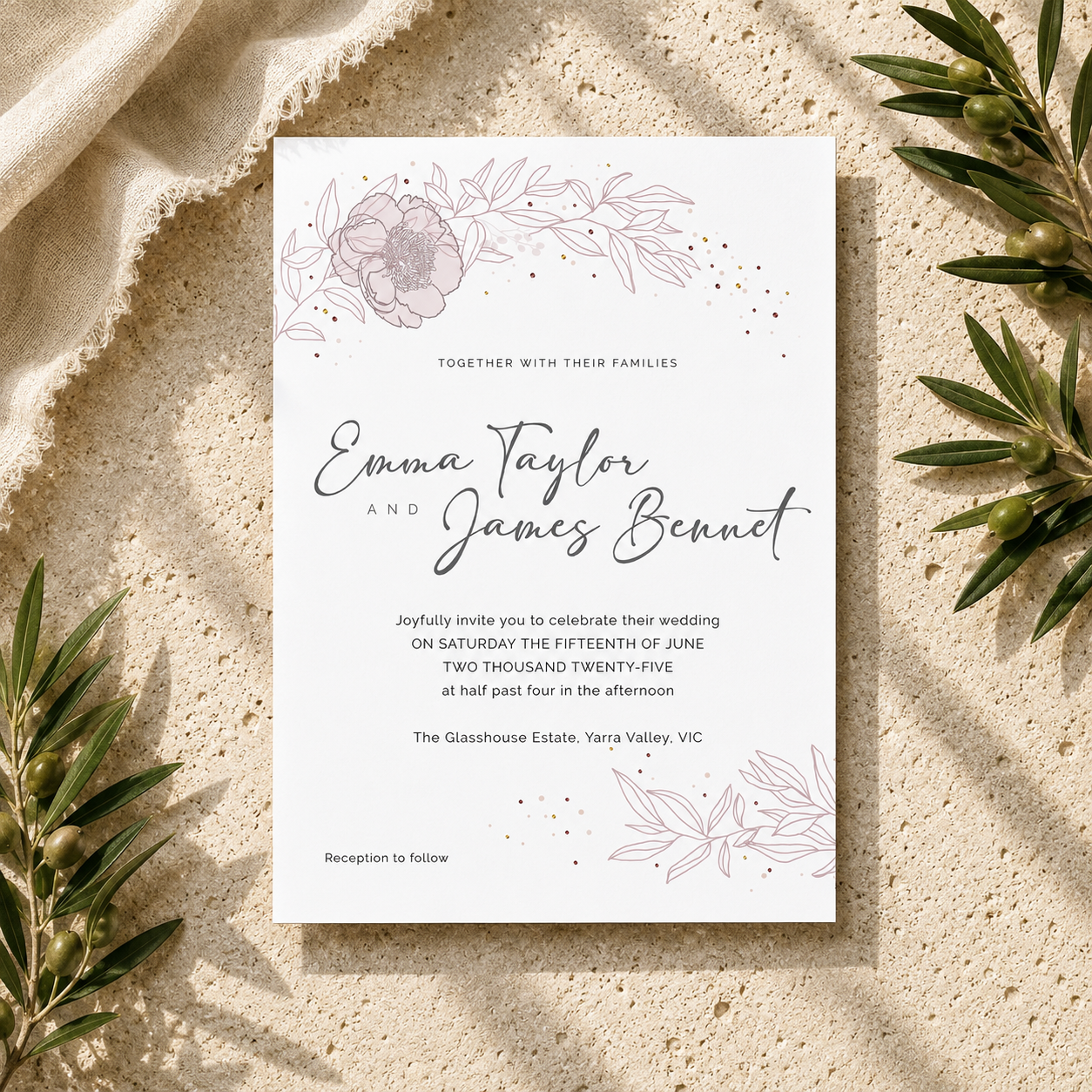 A square wedding invitation card with elegant black script and delicate floral line art, styled flat-lay on a textured beige stone surface with olive branches and draped fabric.