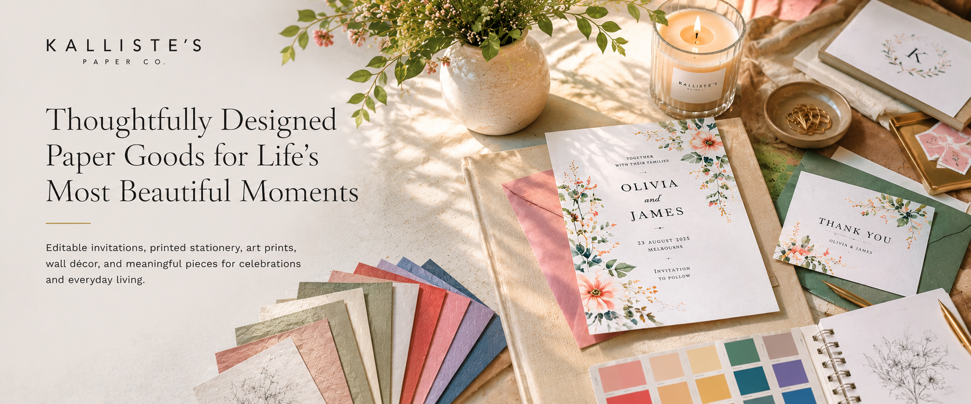 A styled flat-lay of Kalliste's Paper Co. paper goods, including floral invitation cards, a thank you card, colorful paper swatches, and a candle, arranged on a neutral background with a warm candlelit aesthetic.