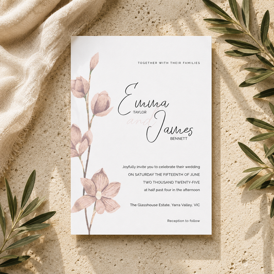 A wedding invitation card with elegant black script and floral illustrations, styled flat-lay on a textured beige surface with linen and olive branches.