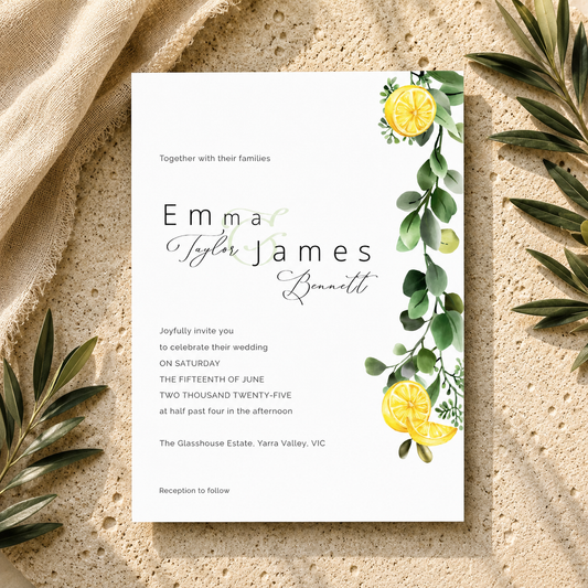 A wedding invitation card with elegant black and cursive text, personalized names, and watercolor lemon and eucalyptus illustrations, styled flat-lay on a textured beige surface with linen and olive leaves.