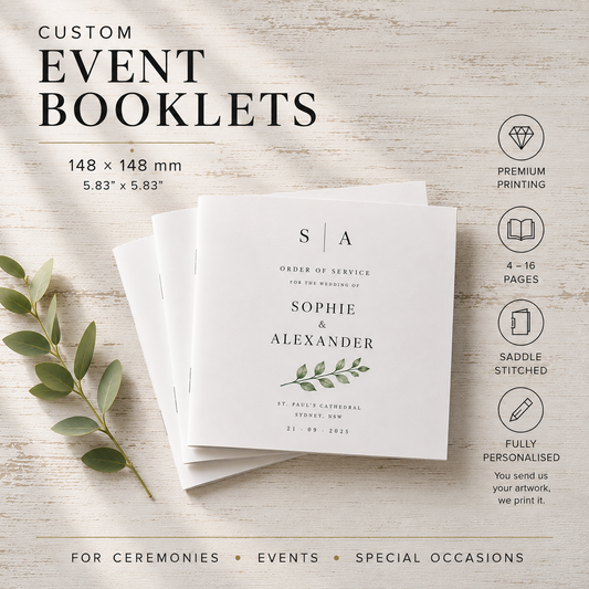 Three custom event booklets for the wedding of Sophie & Alexander are stacked on a light wood background with a green leaf branch. The booklets are white with elegant black typography and a small green botanical illustration.