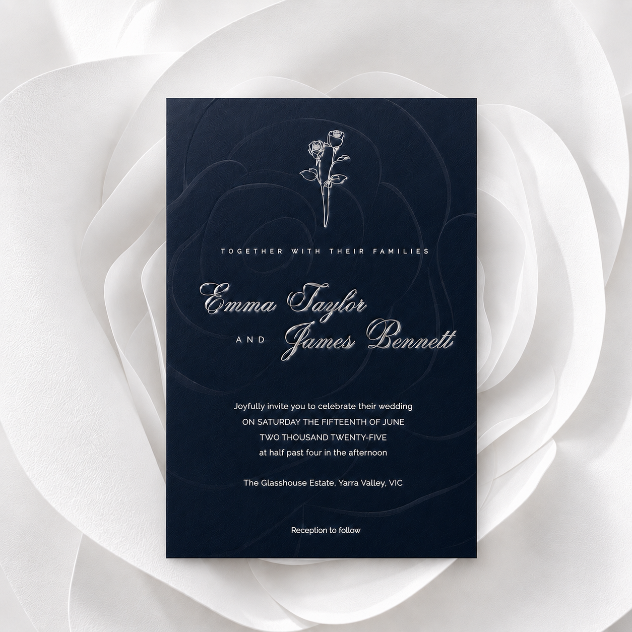 A rectangular navy blue wedding invitation card with elegant white typography and a small rose illustration, centered on a large white fabric rose background.