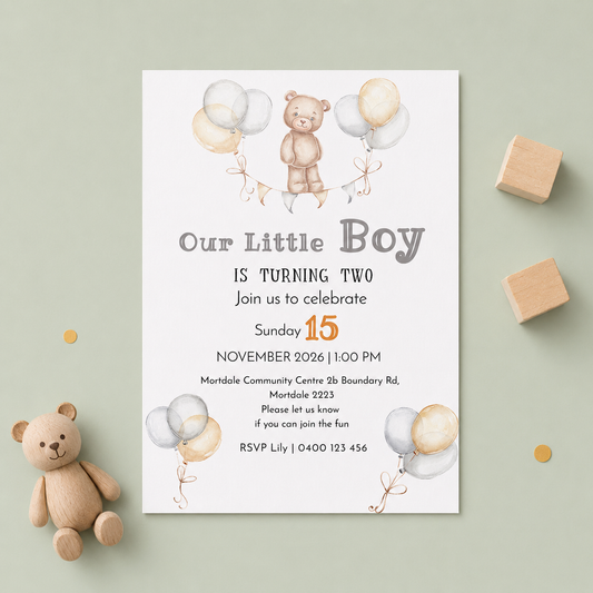 A baby boy's two-year-old birthday invitation card styled in a flat-lay arrangement on a sage green background, surrounded by wooden toy blocks, confetti, and a small teddy bear.