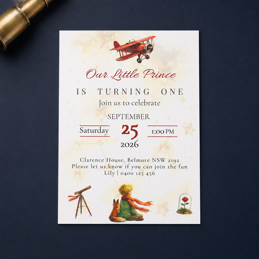 A vintage-style children's first birthday invitation card with a white background, featuring illustrations of a red biplane, a telescope, a teddy bear, and a small flower dome. The card is displayed flat on a dark navy blue surface next to a gold telescope prop.